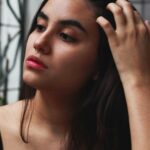 Natural light portrait of a young woman gently touching her hair, set in an outdoor environment.